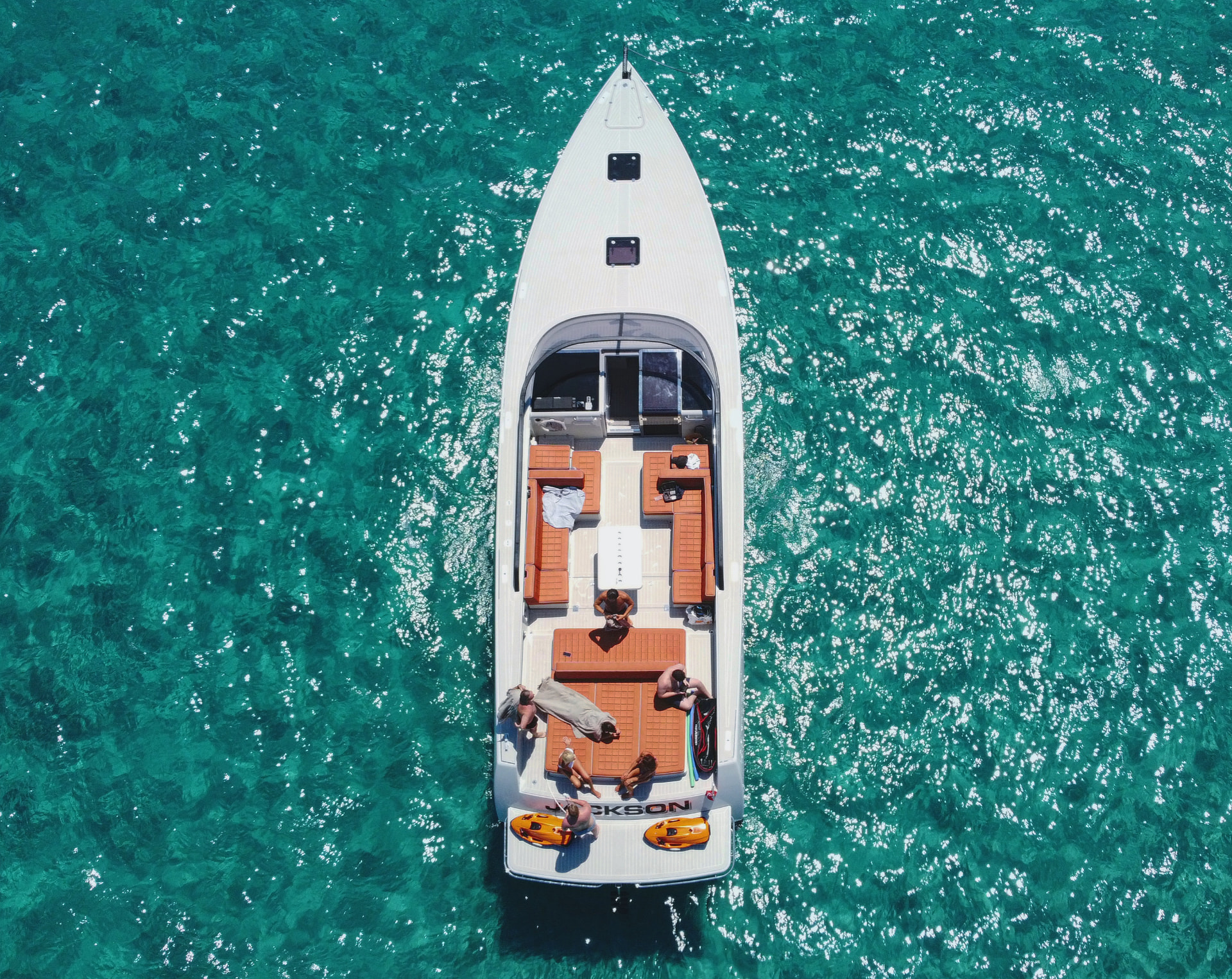 Aerial top-down view of a yacht on turquoise water with people relaxing on deck