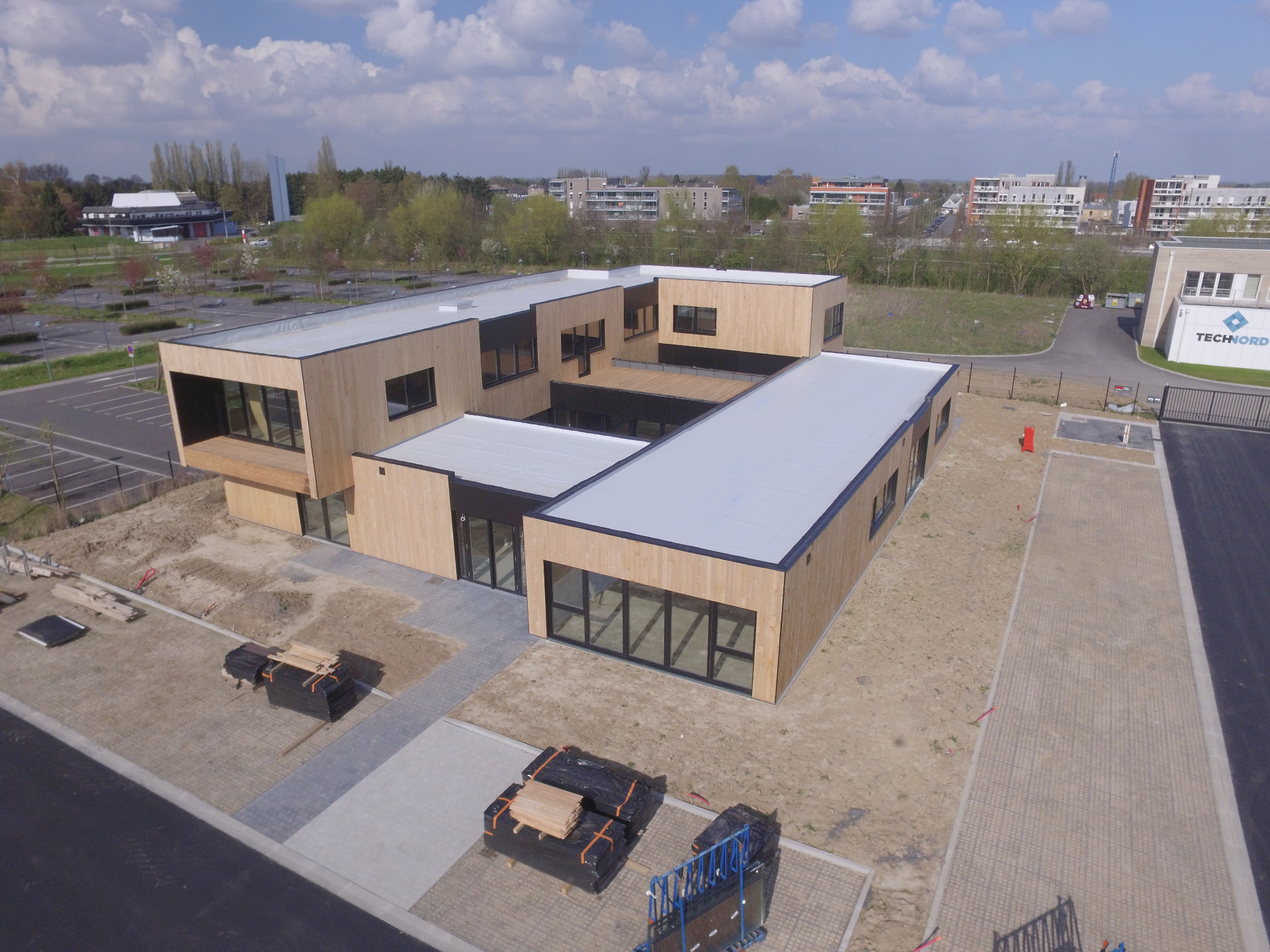 Aerial view of a modern timber-clad building with a flat roof on a developing site
