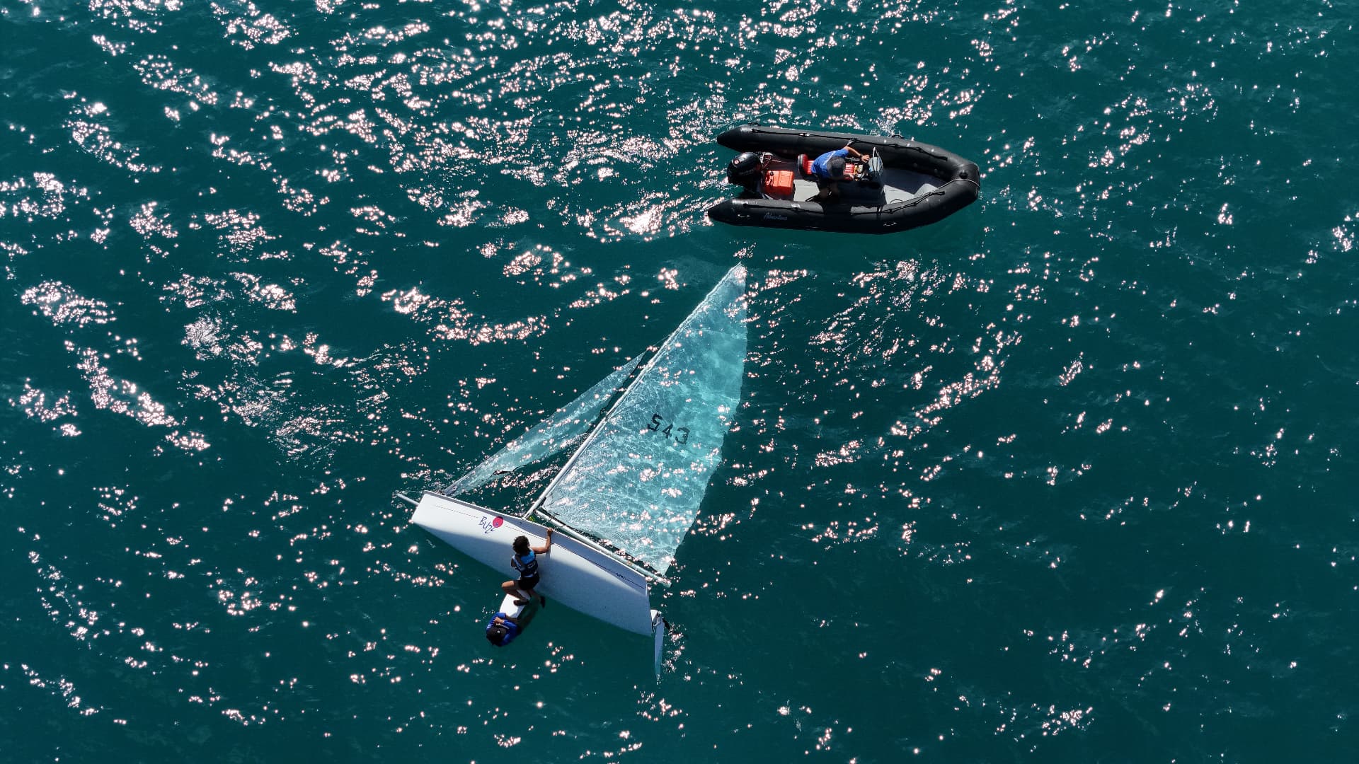 Aerial view of a sailing dinghy and support rib on sparkling blue water