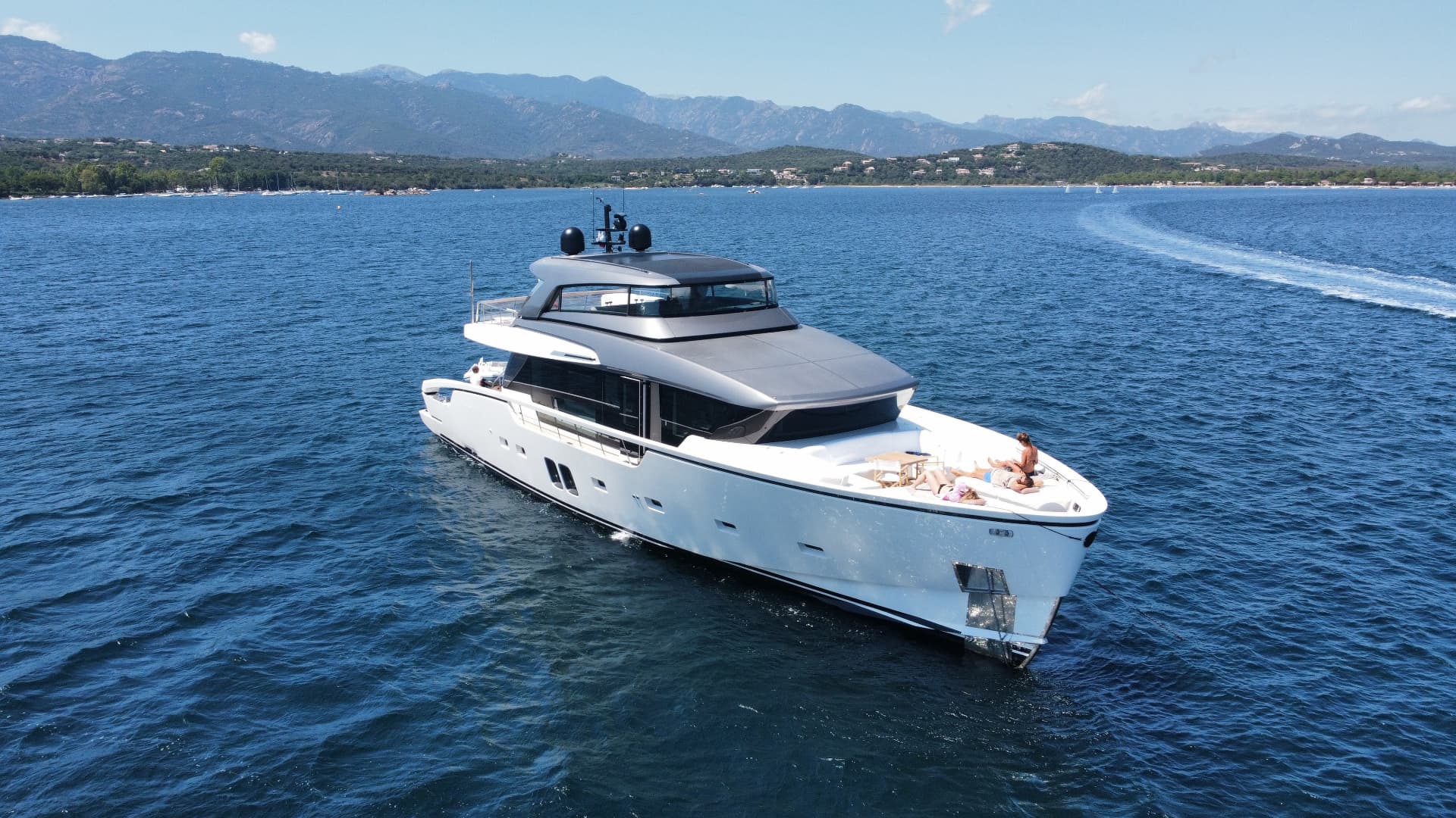 Aerial view of a modern motor yacht cruising in a calm blue bay with mountains in the distance